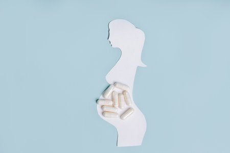 A paper silhouette of a pregnant woman and white pills on a blue isolated background, the end of treatment and during pregnancy and vitaminsの写真素材