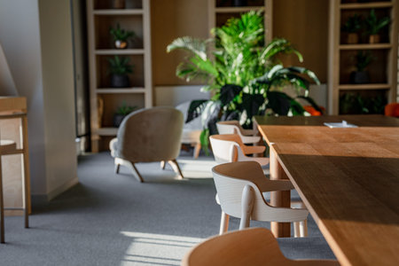 A modern interior of a cafe or coworking space with a long, light-colored countertop in the foreground. There are potted green indoor plants everywhere, and open shelving.の写真素材
