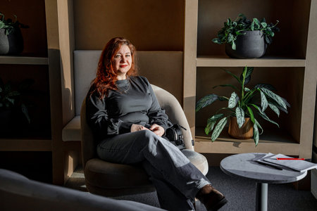 Adult woman is sitting at a wooden cafe table in a beautiful modern room with green plantsの写真素材