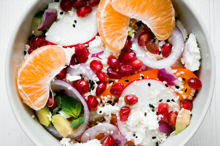 salad with fresh vegetables, feta cheese, garnets and tangerines. healthy diet or vegetarian food on a wooden background. Top view.の写真素材
