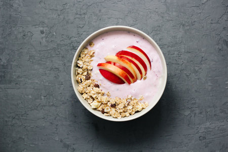 Bowl of oatmeal porridge with blueberry yoghurt, milk and muesli with an apple on concrete background. Organic healthy food or breakfast. lifestyle concept. top viewの写真素材