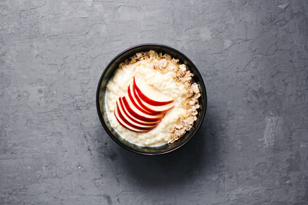 Bowl of oatmeal porridge with blueberry yoghurt, milk and muesli with an apple on concrete...