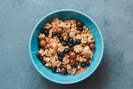 granola or flakes with berries of black currant and gooseberry in a pink plate on a white...