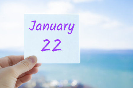 January 22nd. Hand holding sticker with text January 22 on the blurred background of the sea and sky.の写真素材