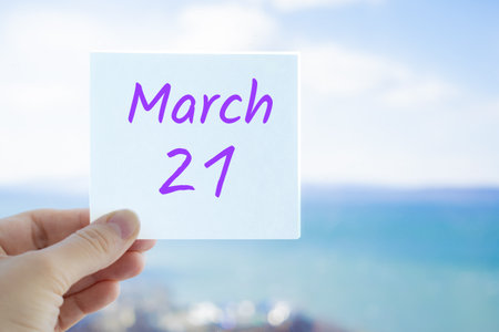 March 21st. Hand holding sticker with text March 21 on the blurred background of the sea and sky. Copy space for text. Spring month in calendar concept.の写真素材