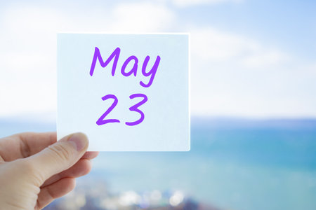 May 23rd. Hand holding sticker with text May 23 on the blurred background of the sea and sky. Copy space for text. Month in calendar concept.の写真素材