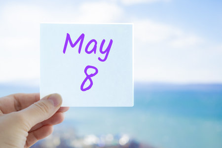 May 8th. Hand holding sticker with text May 8 on the blurred background of the sea and sky. Copy space for text. Month in calendar concept.の写真素材