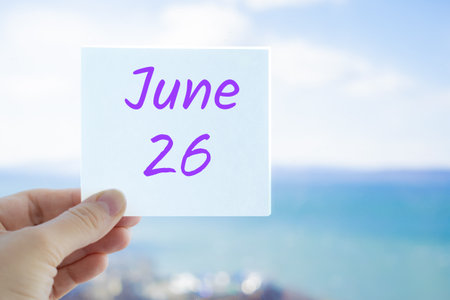 June 26th. Hand holding sticker with text June 26 on the blurred background of the sea and sky. Copy space for text. Month in calendar conceptの写真素材