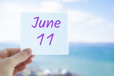 June 11th. Hand holding sticker with text June 11 on the blurred background of the sea and sky. Copy space for text. Month in calendar conceptの写真素材