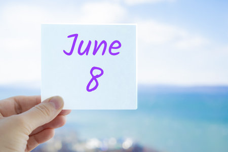June 8th. Hand holding sticker with text June 8 on the blurred background of the sea and sky. Copy space for text. Month in calendar concept.の写真素材