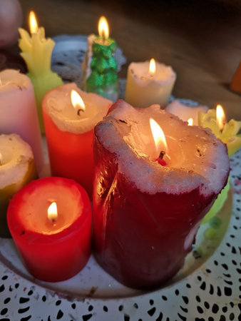 Burning multicolored candles stand on a white platterの写真素材
