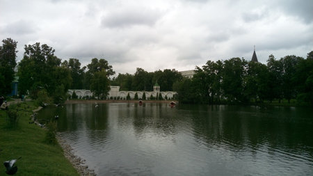 The gray surface of the lake with reflected clouds and white buildings hidden behind green treesの写真素材