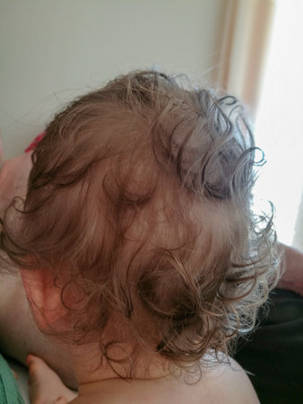 close-up of a baby's head with big brown curls sitting at homeの写真素材