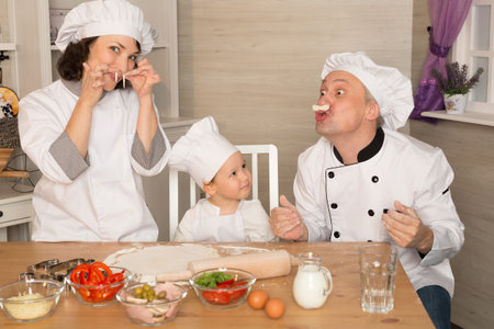 Mom, dad and son cook together from the dough. Teaching a child. Leisure quarantined family. Cheerful family in cook costumes cook pizzaの写真素材