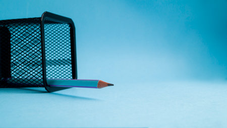 A sharpened simple pencil lies in a mesh jar on a blue background. Sharpened pencil tip. The concept...
