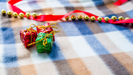 New Year and Christmas card. Christmas decoration plaid in a cage. Three small gifts, gold beads and a red satin ribbon lie on a winter blanket. Place for your text. Copy space. Selective focus.の写真素材