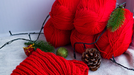 Balls of red thread for knitting in the New Years decor, they have a garland on them. Knitting a Christmas sweater. Preparing to celebrate the new year and christmas. DIY sweater for the holiday.の写真素材
