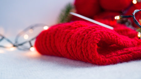 Part of a red knitted product on hand-knitted needles in the New Years decor, consisting of a garland on a light background. Do-it-yourself knitting of a Christmas sweater.の写真素材