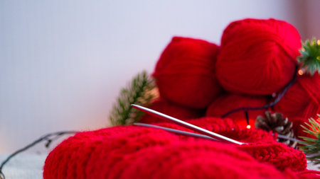 Knitting needles with a red product on the background of balls in the New Years decor. Do-it-yourself knitting of a Christmas sweater. Preparing to celebrate the new year and christmas.の写真素材