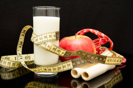 The concept of diet, rope, glass of milk, meter, apple on a black backgroundの写真素材