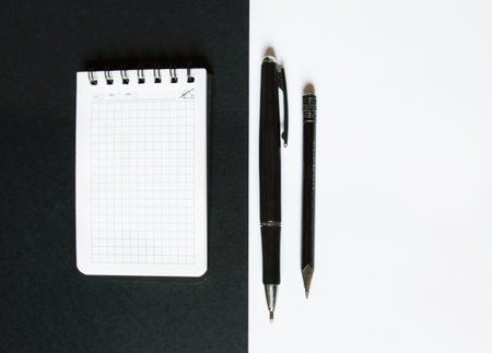 notebook with pencil and pen lie on black and white backgroundの写真素材
