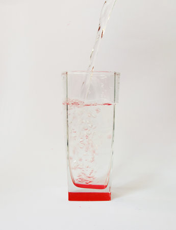 glass beaker with a red bottom with water on a white background. pour water into a glassの写真素材