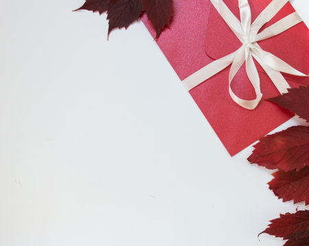 gift red envelope with a white bow. gift on a white background. red autumn leaves. composition of...