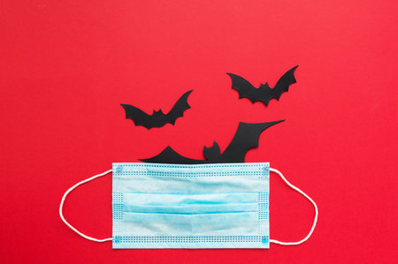 Halloween flat lay - bats, pumpkin on red background. quarantine theme, protective mask. gifts for hallowne.の写真素材