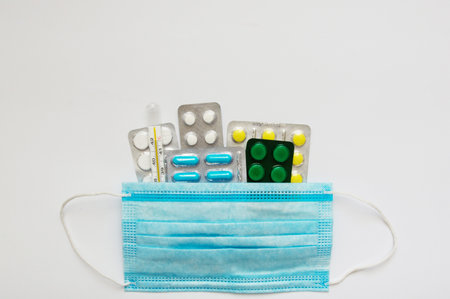 Medical mercury thermometer on the background of pills and a protective mask. Medicinal pills on a...