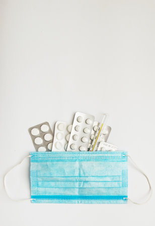 Medical mercury thermometer on the background of pills and a protective mask. Medicinal pills on a white background. Coronavirus and isolation. Medicinal medicine as background.の写真素材