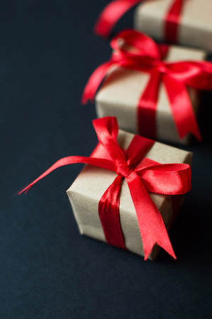 Festive concept - gifts with craft paper with a red bow on a black background. composition for...