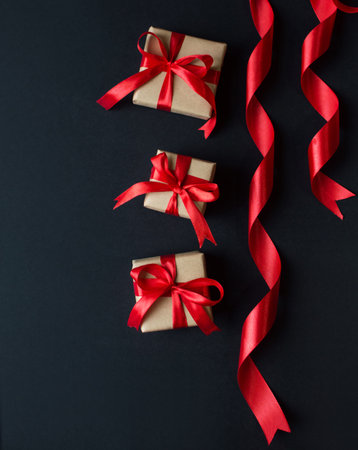 Festive concept - gifts with craft paper with a red bow on a black background. composition for christmas, new year and holidays. flat lay with place for text.の写真素材