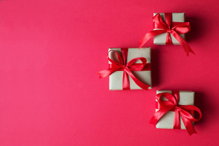 Festive concept - gifts with craft paper with a red bow on a red background. composition for...