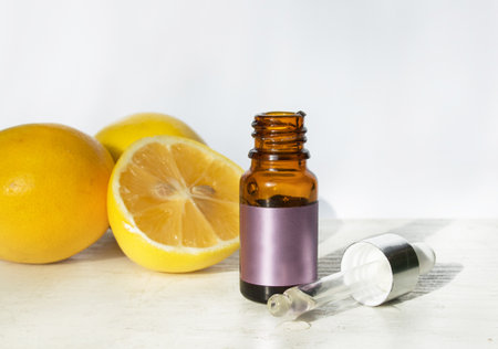 The concept of natural care cosmetics with a bottle of essential oil and serum on a white background and with lemon and green leaves. Flat composition with cosmetic products with place for text.の写真素材