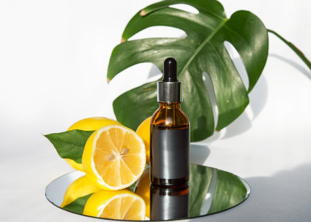 The concept of natural care cosmetics with a bottle of essential oil and serum on a white background and with lemon and green leaves. Flat composition with cosmetic products with place for text.の写真素材