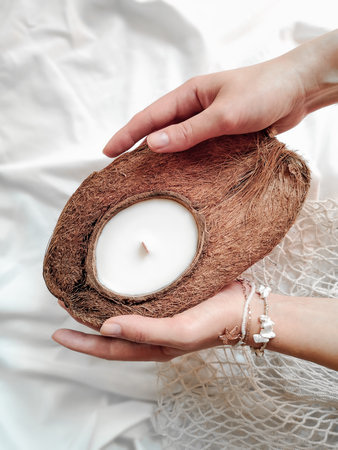 Soy candle in coconut holding in woman hands on white background. close up.の写真素材