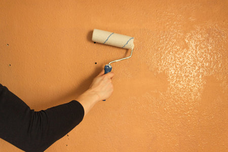 Mans hand holds paint roller and paints the brown wall. Repair and renovation of the home walls.の写真素材