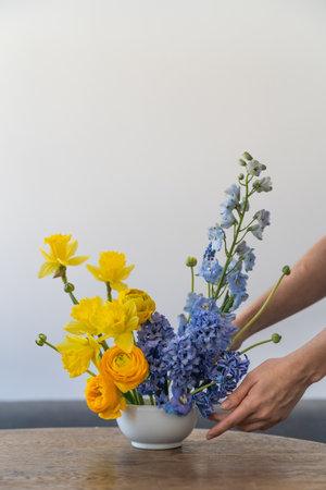 Florist womans hands create flowers arrangement with seasonal spring garden blue and yellow flowers.の写真素材