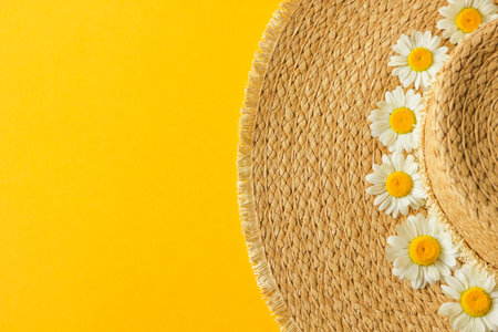 Top view of straw sunhat decorated with daisies chamomile flowers isolated on a yellow background....