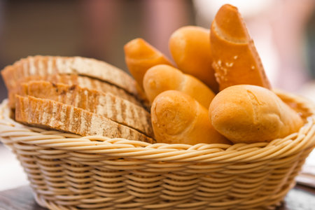Set of different pastries crispy rools, pretzels, beer sticks and freshly sliced bread in a wicker basket on the table.の写真素材