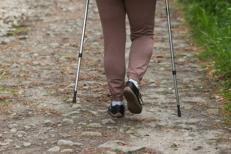 Close up of womans legs with trekking sticks on the rocky road. Nordic walking in mountains forest.