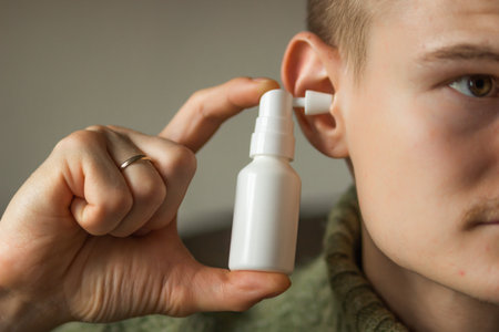 Man uses an ear spray. Mans hand holds a white ear spray bottle with nozzle installed in the ear hole. Daily hygiene.の写真素材