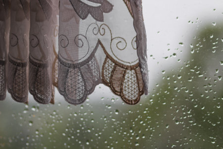 Wet window glass with old vintage grandmas curtains. Rain drops on the window glasses surface with nature background.の写真素材