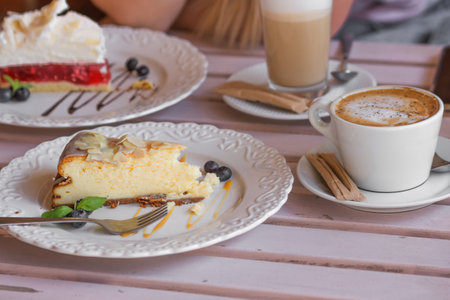Table for two in the street coffee shop. Plate with piece of cheesecake and blueberries, cup of cappuccino and latte.の写真素材