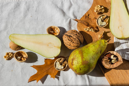 Ripe pears, walnuts, wooden cutting board and dry oak leaves isolated on white fabric background. Healthy eating conceptの写真素材