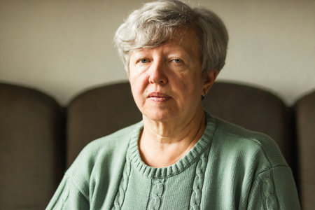 Portrait of a sick caucasian senior woman with short gray hair and headache sitting at home on a...