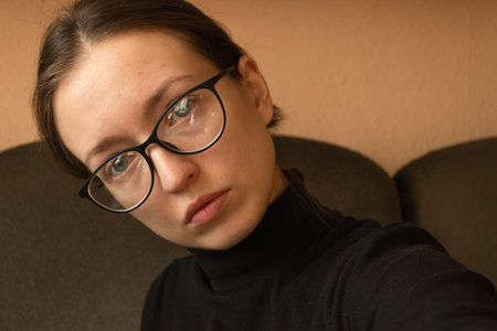 Portrait of a sick caucasian woman in black sweater and glasses, with headache sitting at home on a...