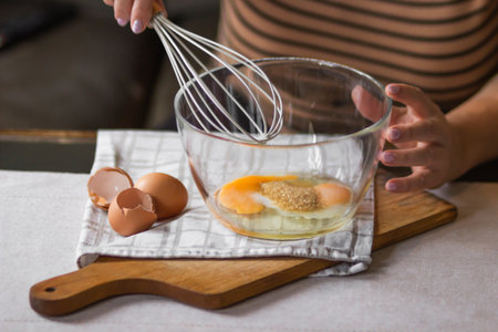 Elderly woman beats eggs with a wisk in a glass bowl. Prepare for making christmas pie or morning...