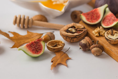 Autumn still-life with ripe figs cut in slices, walnuts and plate full of honey on the wooden cutting board, decorated by dry oak leaves and acorns. Set of organic snacks for wine. healthy eating.の写真素材