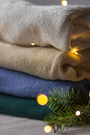 Folded knitted sweaters of different colors perfectly stacked in a pile with fir branch and bokeh lights. Female wardrobe for winter or autumn cozy days. Holiday shopping and sale concept. Xmas vibe.の写真素材
